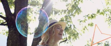 güzel genç esmer kız güneşli parkta sabun köpüğü esiyor.