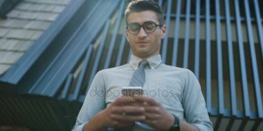 Genç adam cep telefonuyla ofis binası önünde Beyaz gömlekli 