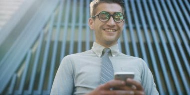 Genç adam cep telefonuyla ofis binası önünde Beyaz gömlekli 