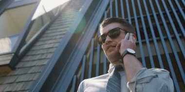 yakışıklı işadamı tutarak ve akıllı telefon açık modern bina arka plan üzerinde kullanarak güneş gözlüğü