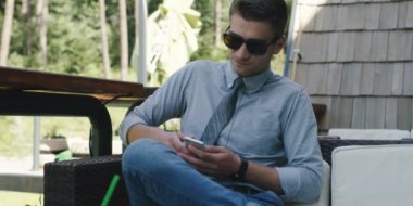 yakışıklı işadamı tutarak ve akıllı telefon açık kafede kullanarak güneş gözlüğü