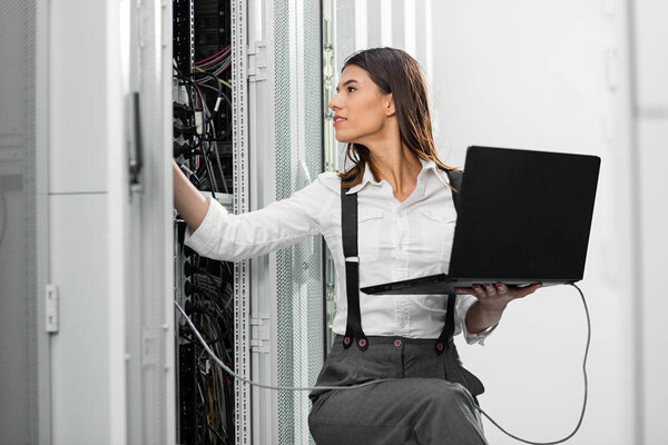 Young expert tehnician fixing an problem through the laptop in server room