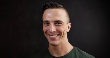 Kameraya gülümseyen genç adam. Siyah arka plan. Açık yüz