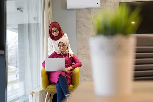 Two women with hijab working on laptop in modern office.