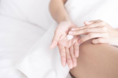 Kadın beyaz yatağa nemlendirici krem / losyon sürüyor, güzellik konsepti.