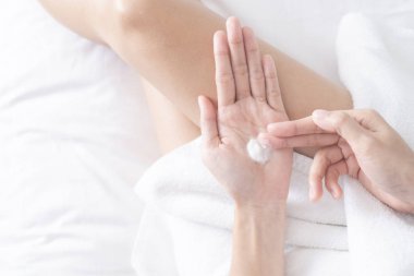 Kadın beyaz yatağa nemlendirici krem / losyon sürüyor, güzellik konsepti.