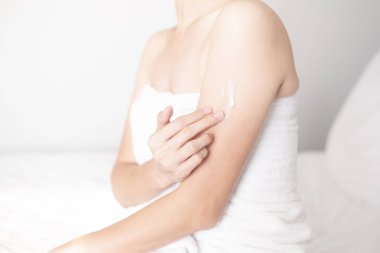 Bilek kremi süren bir kadın, beyaz yatakta losyon süren bir kadın, hijyen cilt bakımı konsepti.