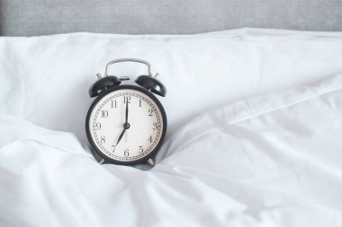 Taklit alanı olan beyaz yataktaki alarmlı saat.