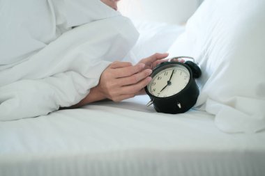 Yatakta uyuyan bir kadın çalar saati kapatır ve sabah uyanır, seçici bir şekilde odaklanır.