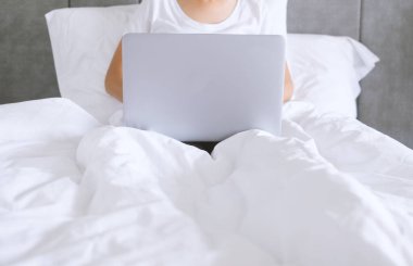 Yatakta çalışmak için dizüstü bilgisayar kullanan bir kadın. Ev kavramından.