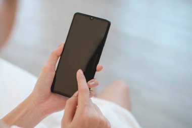 Kadın banyodan sonra elinde boş ekran akıllı telefonuyla yatakta oturuyor. Teknoloji kavramı..