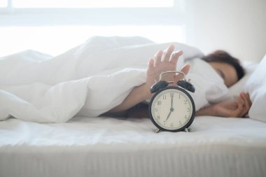 Yatakta uyuyan bir kadın çalar saati kapatır ve sabah uyanır, seçici bir şekilde odaklanır..