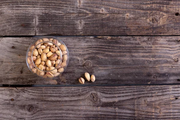Gri ahşap kurullarında bir cam vazo içinde sunulan fotoğraf Antep fıstığı. 