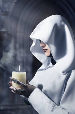 Kalenin içinde yanan bir mum ayakta tutan beyaz kukuletalı pelerin içinde büyücü. Profil görünümü fotoğraf.