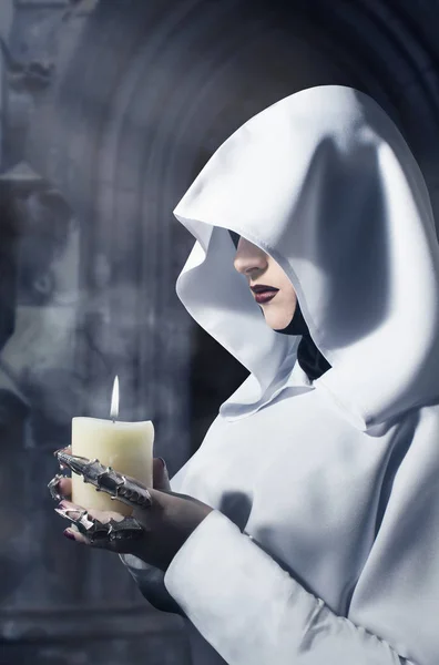 Kalenin içinde yanan bir mum ayakta tutan beyaz kukuletalı pelerin içinde büyücü. Profil görünümü fotoğraf.