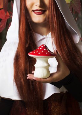 Pretty smiling redheaded girl holding an amanita mushroom on autumn nature background. clipart