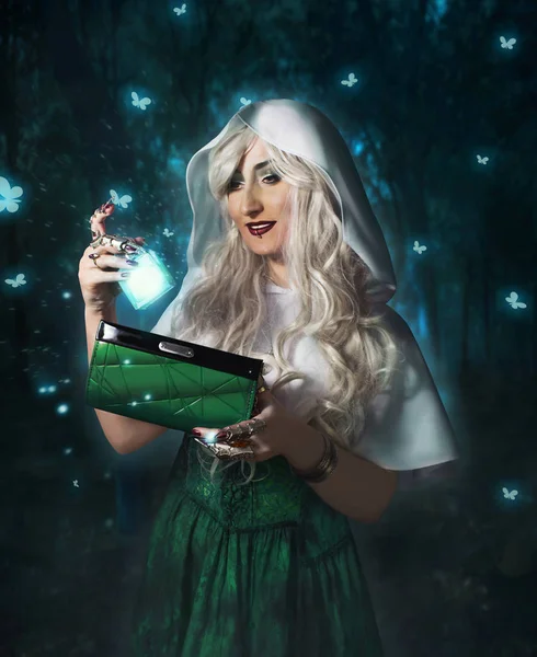 Beautiful smiling fantasy woman holding the vial of magical potion and cosmetic bag standing in the night forest with glowing butterflies.