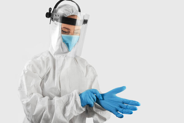 Isolated young woman in medical uniform and mask putting on a medical glove. Healthcare and medical concept.