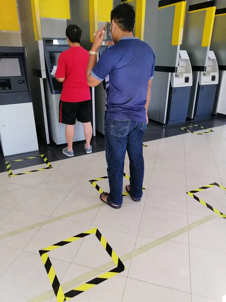 People queueing in line front of bank atm counter by following the safety guideline due to coronavirus pandemic .COVID-19 safe social distancing practice, financial crisis,banking,loans.