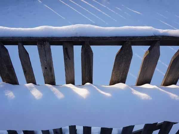 snow on an old wooden fence, illuminated by the sun.