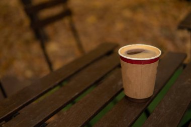 Tahta bir masanın üzerinde bir bardak var. Kahveyi ağaçların arasına döktü.
