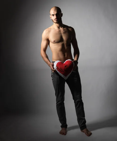 Bodybuilding and Health: handsome strong bodybuilder holding a paper card red heart isolated on a white background in studio