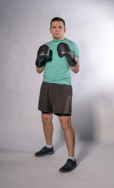Boxeador profesional en guantes negros con pantalones cortos en fondo de altura completa gris y blanco —  Fotos de Stock