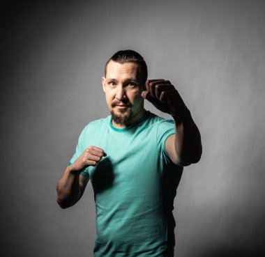 Deneyimli boksör boks tekniklerini gri arka planda, bıyıklı ve sakallı bir tişörtle gösteriyor.