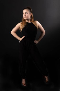 Kız siyah arka planda, canlı siyah giysiler içinde yan tarafa bakıyor.