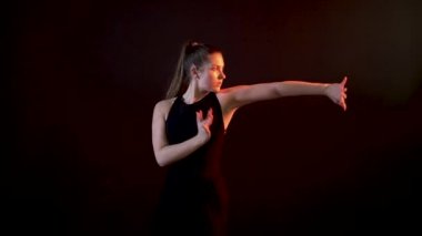 Siyah arka planda güzel dans eden bir kız. El sallayan bir balo salonu, plastik.