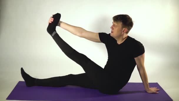 Розтягування ніг в положенні за п'ятою, на білому тлі в чорних тренувальних штанах — стокове відео