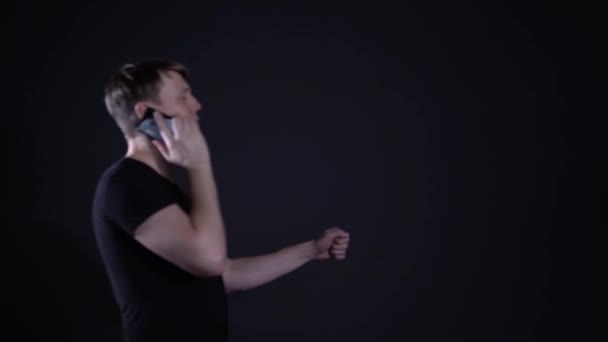 Молодой человек разговаривает по телефону на черном фоне и водит машину — стоковое видео