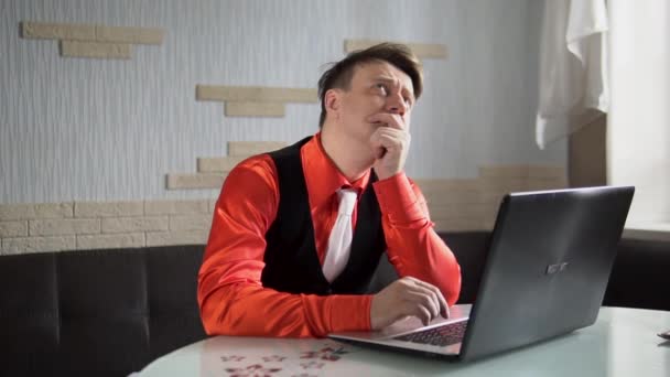 一个男人梦想着坐在笔记本电脑前，坐起来，一只手放在下巴上，一件红色的衬衫 — 图库视频影像