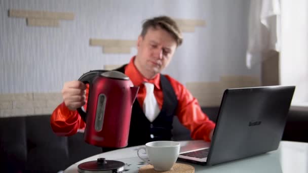 Schenkt thee man, achter een laptop in een rood shirt en in een witte das — Stockvideo