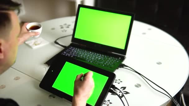 Artistas portátiles y tabletas con pantallas verdes en la mesa en la cocina de la casa — Vídeos de Stock