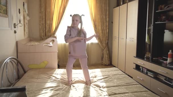 Een meisje danst boogie vugi thuis op een bed in fel licht, in beige pejama. — Stockvideo