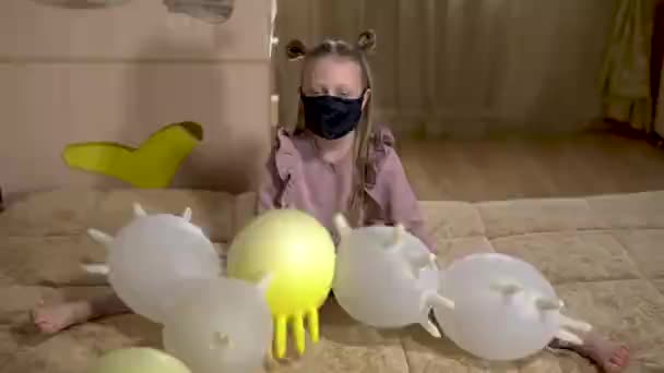 Avec des gants gonflables joue une fille, dans un masque médical, à cause du coronavirus Covid19. Étaient assis à la maison — Video