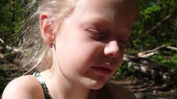 A girl of European appearance 8 years old, eats an apple and watches a tablet in the woods. — Stock Video