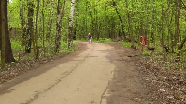 På en cykel rider en flicka och viftar med handen glad, ler — Stockvideo