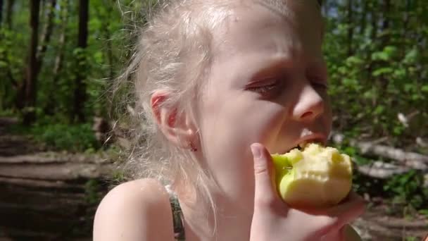 Europäisch aussehendes Mädchen 8 Jahre alt, isst einen Apfel im Wald und schaut auf das Telefon. — Stockvideo