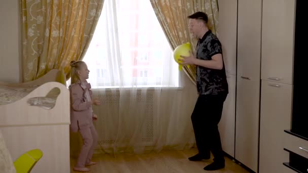 Een vrolijke volwassene speelt handschoenballen met een vrolijke lieve baby in een kinderkamer in modieuze kleding. Op tegen de wieg en bank. — Stockvideo