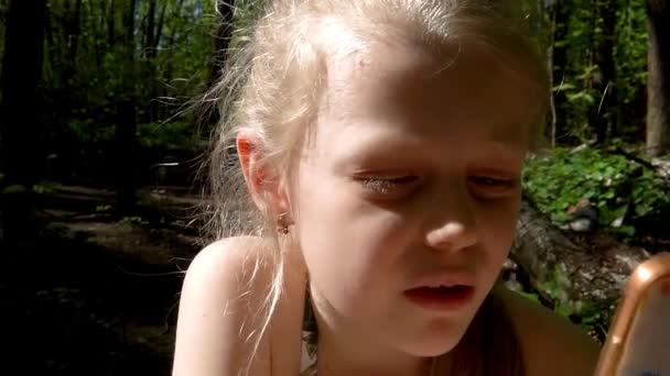 Apple isst ein kleines Mädchen von europäischem Aussehen, blond mit blauen Augen und schaut auf das Telefon. — Stockvideo