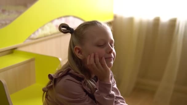 En grubblande liten flicka sitter på en loft säng stege, och tänker igen nära en gul barnsäng, mitt i ett soligt fönster — Stockvideo