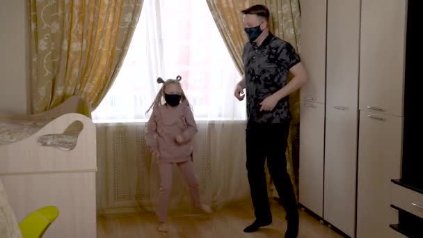 Vreugdevolle volwassen vader danst met een mooi meisje een aansteker in een kinderkamer in huiskleding. Tegen de wieg en de bank. Ze zijn gemaskerd. — Stockvideo