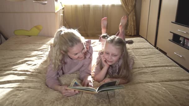 Os dois sorriem, mãe e filha, lendo um livro no berço em uma sala de luz . — Vídeo de Stock