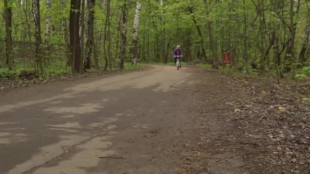 A girl rides a bicycle through a forest park and sings a joyful song — Stock Video