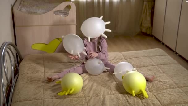 Veselá dívka si hraje s balónky s rukavicemi v krásném bytě na měkké pohovce se žlutými rukavicemi a bílými balónky. ve světlé místnosti. — Stock video