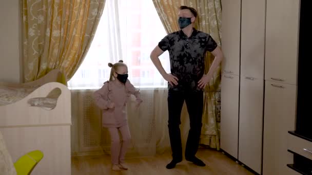 En glad ung kvinna dansar med en glad infödd bebis i ett stort vardagsrum i hemkläder. Mot ett ljust fönster. De är maskerade. — Stockvideo