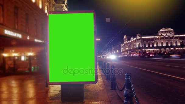 En skylt med en grön skärm på en kväll gator — Stockvideo