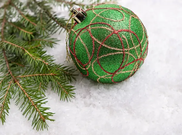 Green Christmas ball and branch against the snow. — Stock Photo, Image